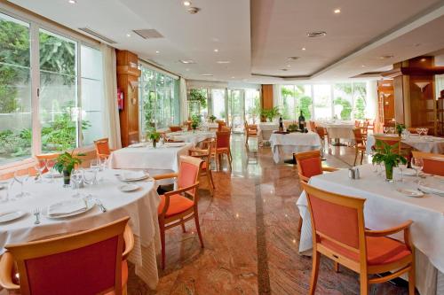 un restaurante con mesas y sillas blancas y ventanas en VP Jardín de Tres Cantos, en Tres Cantos