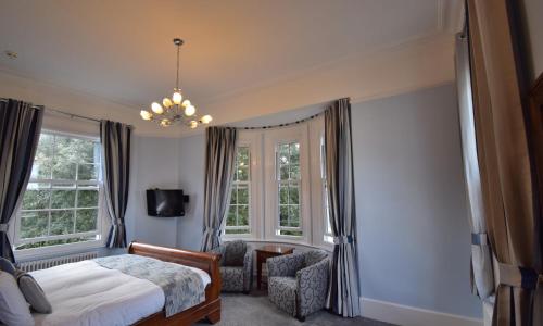 a bedroom with a bed and a chair and windows at Lincombe Hall Hotel & Spa - Just for Adults in Torquay