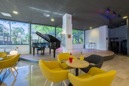 a living room with yellow chairs and a piano at Hotel California Palace in Salou