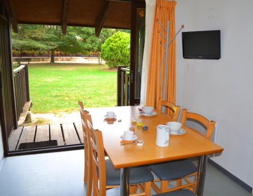 une table en bois avec des chaises et une télévision sur une terrasse couverte dans l'établissement VVF Dordogne Lot, à Gluges