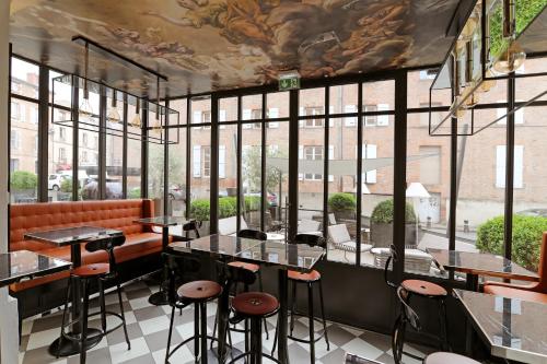 a restaurant with tables and stools in front of windows at Hôtel Alchimy in Albi