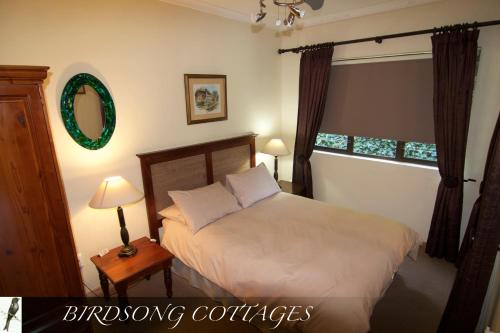 ein Schlafzimmer mit einem Bett, zwei Lampen und einem Spiegel in der Unterkunft Birdsong Cottages in Champagne Valley