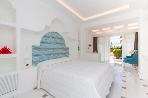 a white bedroom with a white bed and a blue chair at Quattro Passi Relais in Nerano