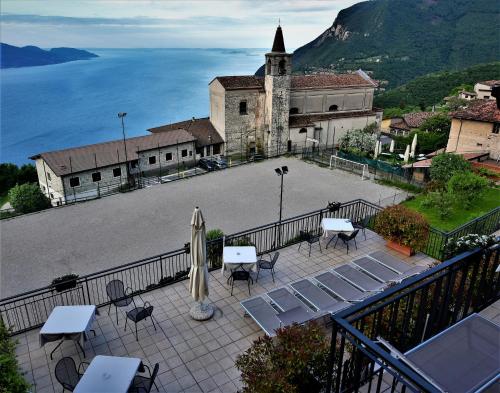 a patio with tables and chairs and a church and water at Hotel Gallo in Tignale