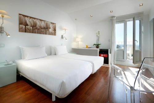 a white bedroom with a large white bed and some windows at Exe Victoria Palace in San Lorenzo de El Escorial