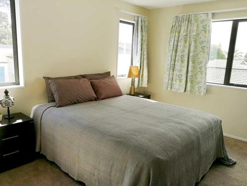 a bedroom with a large bed and two windows at Stunning Stay In Glen Eden Auckland in Auckland