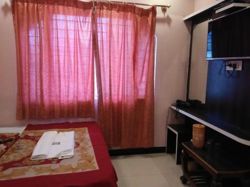 a room with a bed with a red curtain and a television at hotel sangeeth lodging in Mysore