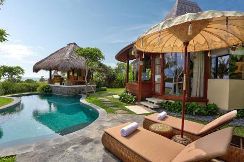 a villa with a pool and chairs and an umbrella at WakaGangga in Tabanan