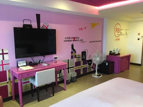 a room with a pink wall with a tv and a desk at R8 Eco Hotel in Kaohsiung