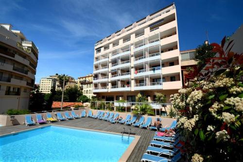 un hôtel avec une piscine, des chaises et un bâtiment dans l'établissement Vacances Cannoise, mer et piscine, à Cannes