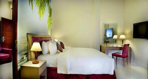 a hotel room with a white bed and a desk at Kuta Central Park Hotel in Kuta