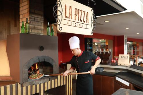 a chef putting a pizza into a pizza oven at Swiss-Belinn Panakkukang in Makassar