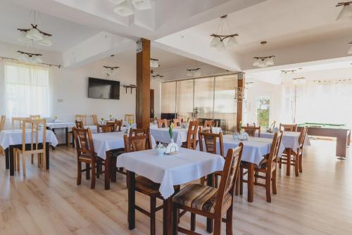 una sala da pranzo con tavoli bianchi e sedie in legno di Ramzes a Ustka