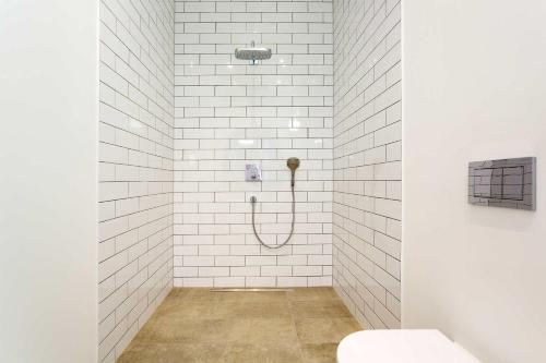 a shower with a hose in a white tiled bathroom at Veeve - Contemporary Studio in Swiss Cottage in London