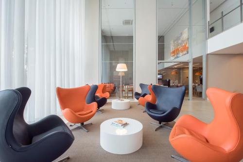 a lobby with orange and blue chairs and a table at Intercity Ribeirão Preto in Ribeirão Preto