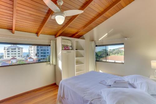 a bedroom with a bed with a ceiling fan and two windows at Pousada Praia dos Ingleses in Florianópolis