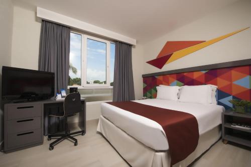um quarto com uma cama, uma secretária e uma televisão em Novus Plaza Hodelpa em Santo Domingo