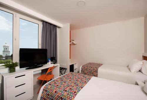 Habitación de hotel con 2 camas y escritorio con TV. en Novus Plaza Hodelpa, en Santo Domingo