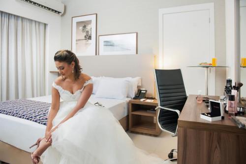 a woman in a wedding dress sitting on a bed at Matiz Multi Suites in Duque de Caxias