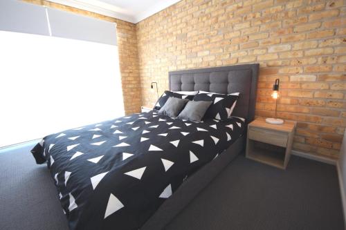 a bedroom with a black and white bed and a brick wall at Ocean Shores Unit No 4 - 48 Paragon Avenue South West Rocks in South West Rocks