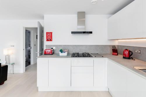 a white kitchen with white cabinets and red appliances at Roomspace Serviced Apartments- Walpole Court in Ealing