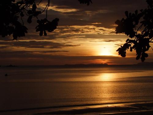 a sunset on the beach with a boat in the water at Baan Suan Kayoo 2 Buffalo Bay Aow Khao Kwai in Ko Phayam