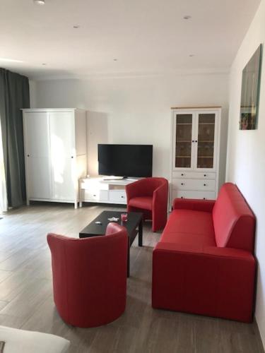 a living room with a red couch and two red chairs at Wassersport-Appartements am Stößensee in Berlin