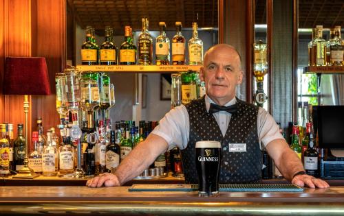 a man standing behind a bar with a drink at Abbeyglen Castle Hotel in Clifden