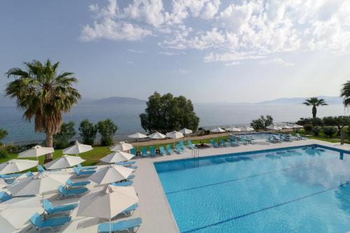 a pool with umbrellas and chairs and the ocean at Calamos Beach Family Club in Kalamos