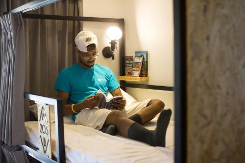 a man sitting on a bed looking at his cell phone at Light Hostel - Tainan in Tainan