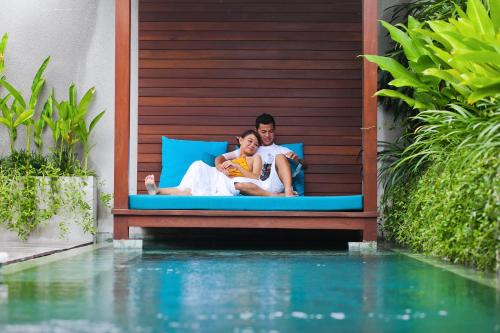 a man and woman sitting on a bed next to a swimming pool at Maca Villas & Spa Bali in Seminyak