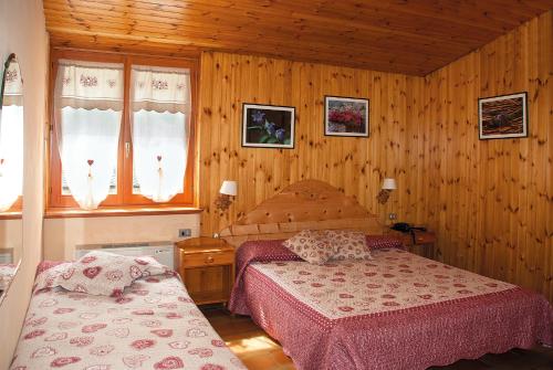 a bedroom with two beds and wooden walls and windows at Hotel Corona in Branzi