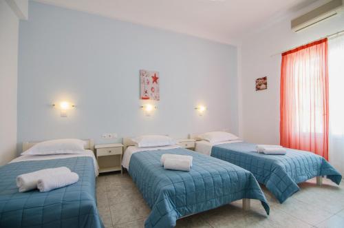 three beds in a room with blue comforters at Athena Rooms in Ios Chora