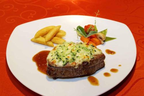 a white plate with a piece of meat and french fries at Zedernhof Gesundheits- & Wellnesshotel in Stamsried