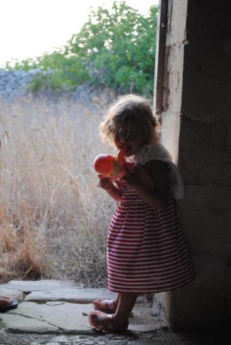 a little girl standing against a wall eating a bottle at Borgoterra in Martano