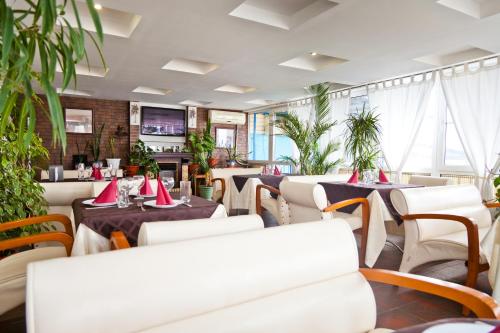 un restaurante con mesas blancas, sillas y plantas en Tornado Hotel, en Yeysk