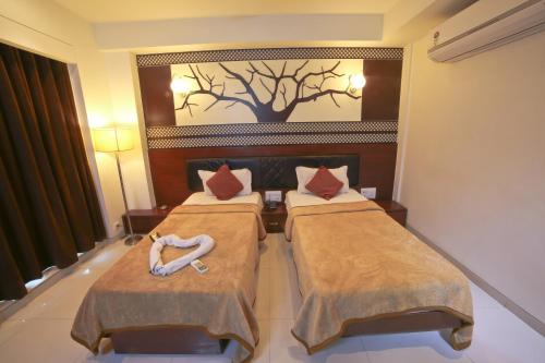 a hotel room with two beds and a tree on the wall at Hotel Grand Pragati in Surat
