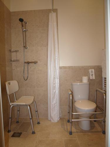 a bathroom with a shower and a toilet and chairs at The Barn and Pinn Cottage in Sidmouth