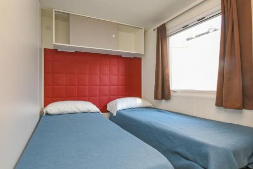 two beds in a room with a window and red wall at Campeggio del Garda in Peschiera del Garda