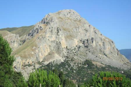 a large rocky mountain with trees in front of it at Ambra di mare in SantʼAgata di Militello