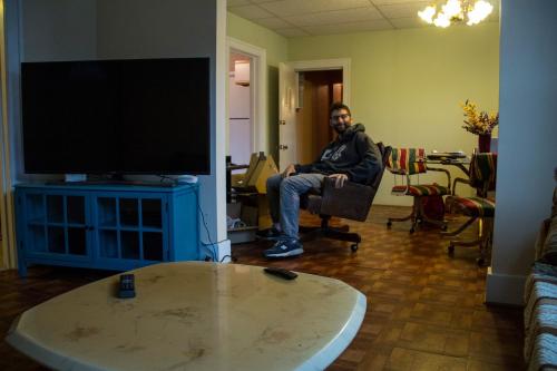 a man sitting in a chair in a living room with a television at Hamtramck Hostel in Detroit