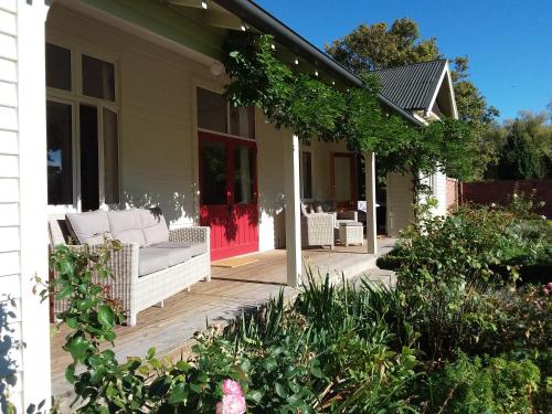 a porch with white wicker chairs and a red door at Hurunui Homestead Bed and Breakfast in Hawarden