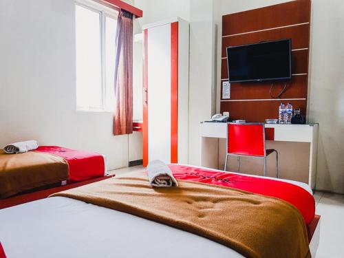a bedroom with two beds and a desk and a television at RedDoorz Plus at Grand City Inn Makassar in Makassar