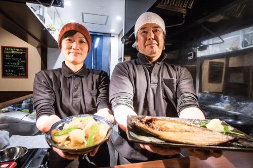 two people standing in a kitchen holding plates of food at SnowDog Village in Niseko