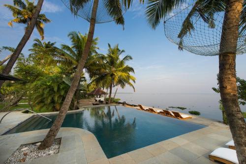 a swimming pool with palm trees and the ocean at Purity at Lake Vembanad in Mararikulam