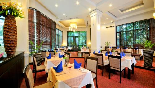 a restaurant with white tables and chairs and windows at Tara Angkor Hotel in Siem Reap