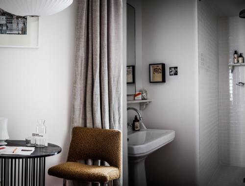 ein Badezimmer mit einem Waschbecken, einem WC und einem Stuhl in der Unterkunft Le Pigalle, a Member of Design Hotels in Paris