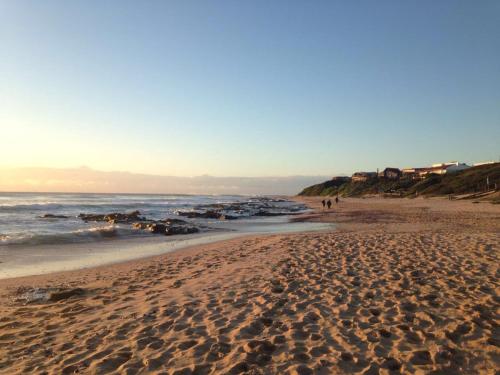 a sandy beach with people walking on the beach at Aloe Again in Jeffreys Bay