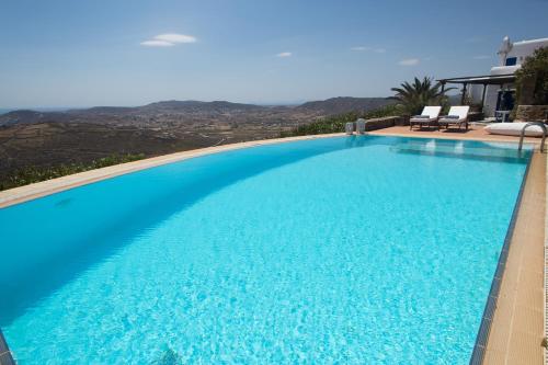 a large blue swimming pool with two chairs on a house at Panorea Complex - Mykonos in Ano Mera