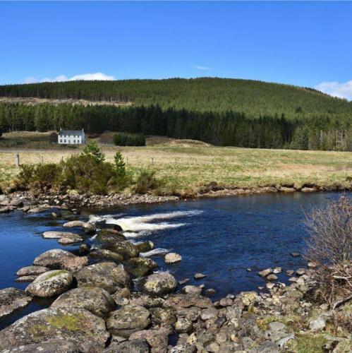 a river with rocks and a house in a field at Knocklea in Alness